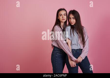 Young women having fun in the studio with pink background. Adorable twins Stock Photo