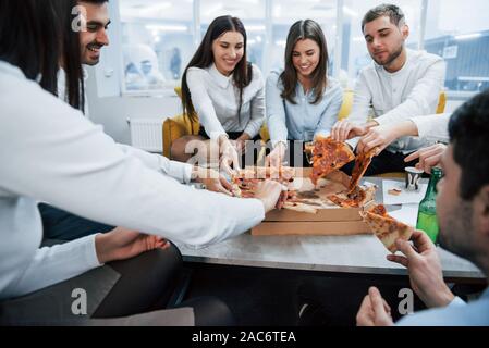 Eating pizza. Celebrating successful deal. Young office workers sitting near the table with alcohol Stock Photo