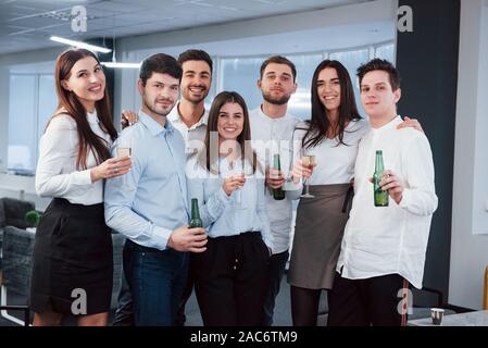 Having good time. Photo of young team in classical clothes holding drinks in the modern good lighted office Stock Photo