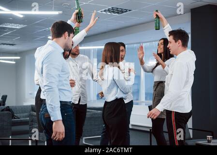 Making a toast. Photo of young team in classical clothes celebrating success while holding drinks in the modern good lighted office Stock Photo