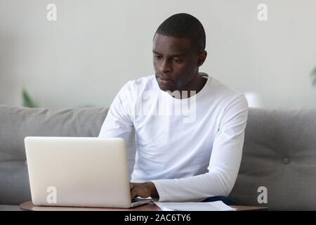 Concentrated serious millennial african american guy working with laptop. Stock Photo