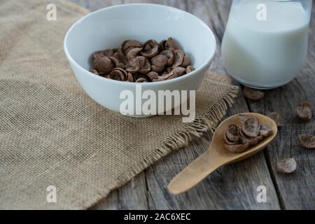 Chocolate-flavored cornflakes in a spoon and milk on the table. Hasty breakfast concept. Stock Photo