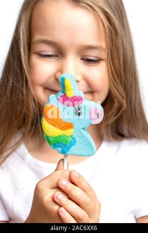 Joyful, happy child holds a unicorn lollipop in his hand on a white background. Close-up trend. Stock Photo