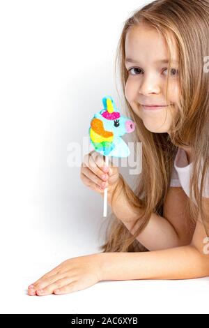 Joyful, happy child holds a unicorn lollipop in his hand on a white background. Close-up trend. Stock Photo