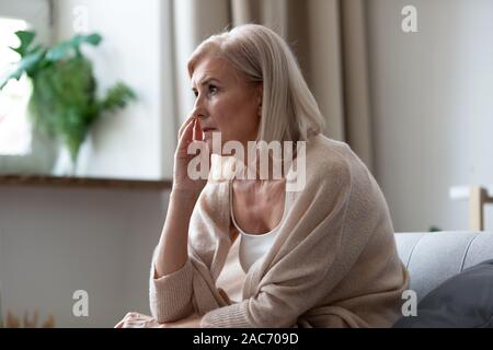 Pensive middle-aged woman seated on couch lost in thoughts Stock Photo