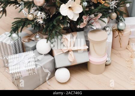 Bright silver gifts in packaging and with bows under the Christmas tree on the floor. Christmas decorations. Christmas background. Beautiful holiday decorated room with Christmas tree with presents under it. Stock Photo