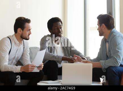 Multi-racial businessmen negotiating seated on couch in office Stock Photo