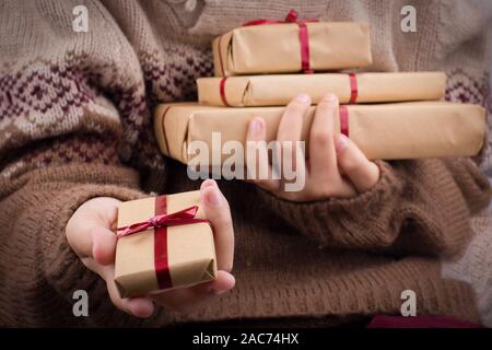 Hand holds out a gift box. Girl in a knitted sweater holds a stack of gift boxes in a brown craft paper. Stock Photo