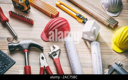 Construction, house renovation concept. Hand tools, hard hats and project blueprints on wood, close up view Stock Photo