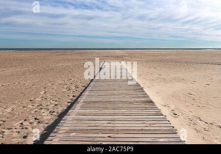 Perspective view of wooden walkway leading to the sandy beach. A blue cloudy sky and the deep blue waters of the ocean in the background. Stock Photo