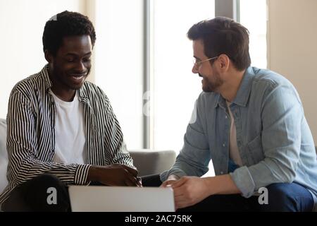 Diverse colleagues sit on couch in office having informal talk Stock Photo
