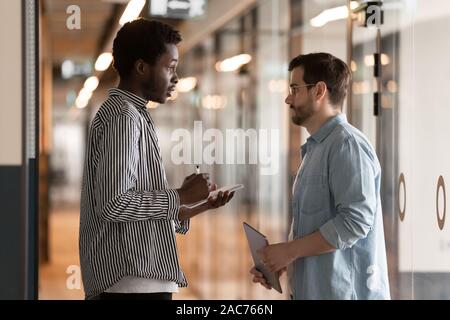 Multi-ethnic colleagues standing in office hallway and talking Stock Photo