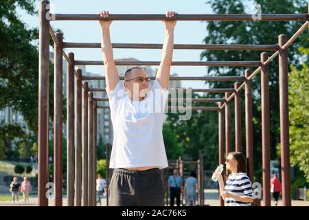 Healthy active lifestyle of age people, middle-aged man doing pull up exercise on horizontal bar outdoor, in city park Stock Photo