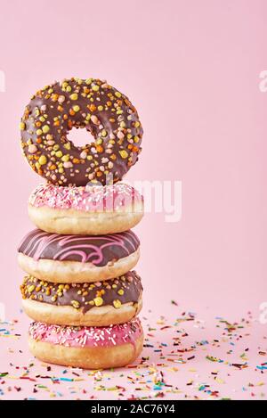 Stack of colorful donuts decorated on pink background Stock Photo