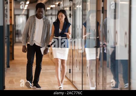 Multiracial workers walk in hallway discuss business opportunities project details Stock Photo