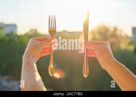 Steel metal shiny knife and fork in a womans hand, background sunset, evening city Stock Photo