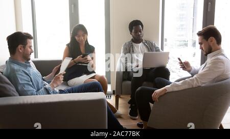 Multiethnic businesspeople rest in office lobby chatting using diverse gadgets Stock Photo