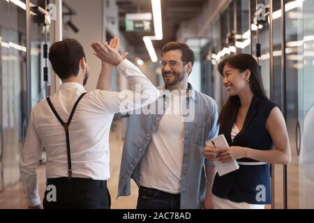 Employees standing in hallway greeting each other giving high five Stock Photo