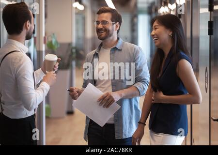 Multiethnic colleagues met in office hallway having informal positive conversation Stock Photo