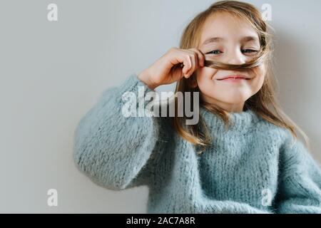 Little girl in a blue sweater playing with her hair, making fake mustache Stock Photo