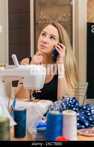 a woman at a sewing machine takes a private order, talking on the phone Stock Photo