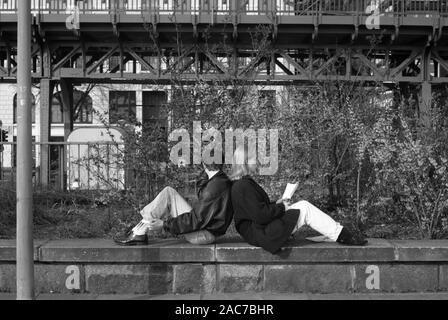 Black and white film photograph of a couple sitting back to back on a low wall, unaware of the camera, on Johannisbollwerk, Hamburg, Germany, circa 1990 Stock Photo