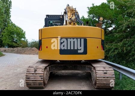 A large yellow excavator visible from the rear, standing on concrete. Stock Photo