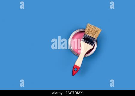 Renovation concept. Blue background with pink paint jar and one brush. Flat lay, top view, copy space. Stock Photo