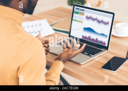 Stressed afro businessman looking at graphs on screen Stock Photo