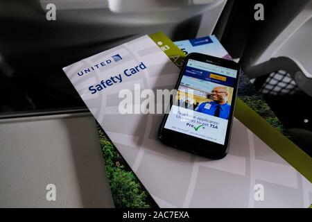 TSA Pre application on the United Airlines Sky Miles Frequent Flyer program phone application; United Safety Card on an airplane tray table. Stock Photo