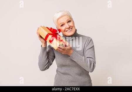 Excited senior woman shaking present box trying guess what inside Stock Photo