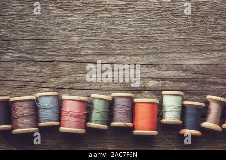 Row of vintage wooden spools of multicolored threads on wooden board. View from above. Copy space for text. Stock Photo