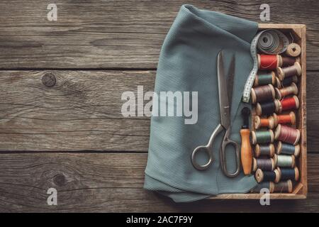 Sewing items: retro tailoring scissors, measuring tape, wooden spools of threads, cutting knife and green cloth in wooden box. Top view. Copy space fo Stock Photo