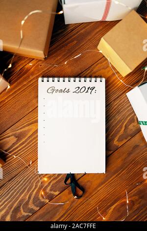 Prepare for Christmas with Notepad and gifts. Notebook with the words Goals 2019 lies on a wooden table. Stock Photo