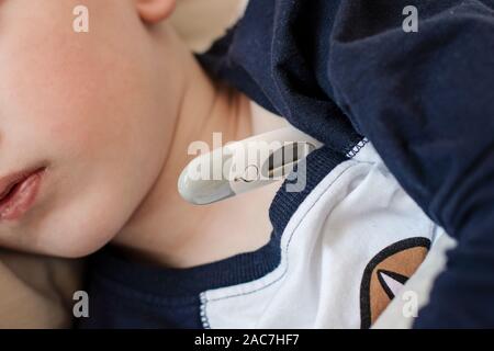 Pre-school sick boy lying on pillow in bed with a digital thermometer. Ill boy is measuring body temperature - close up image Stock Photo