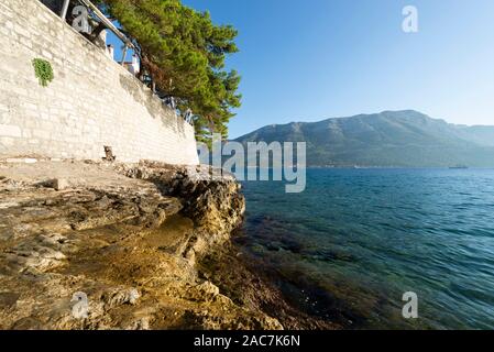 Rocks on the water below the city wall of Korcula with a view of the sea and mountains of Peljesac, Dalmatia, Croatia Stock Photo