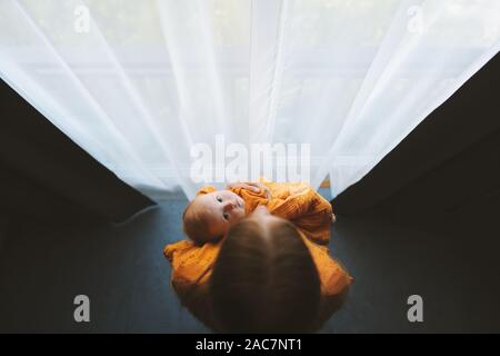 Mother holding baby daughter looking at window family lifestyle mom and infant child together motherhood concept Mothers day holiday view from above Stock Photo