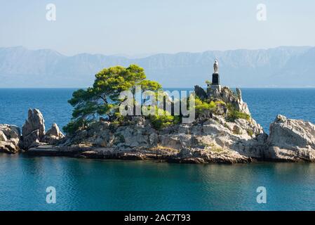 A white Madonna statue stands on a rock in the port of Trpanj against the backdrop of the mountains of the Makarska Riviera, Pelješac,  Croatia Stock Photo