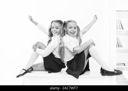 School club. Little schoolgirls classmates friendly kids. Schoolgirls friends sit on desk. Best friends relaxing. Schoolgirls tidy hairstyle relaxing having rest. School uniform. Rebellious spirit. Stock Photo