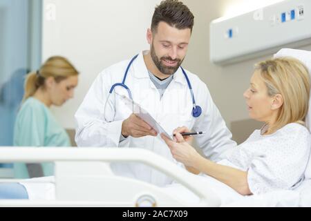 female patient signing paperwork in her hospital bed Stock Photo