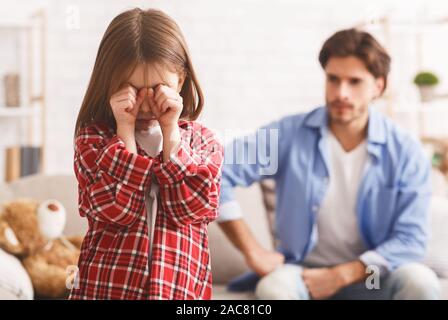 Little girl crying after arguing wIth dad, angry father behind Stock Photo