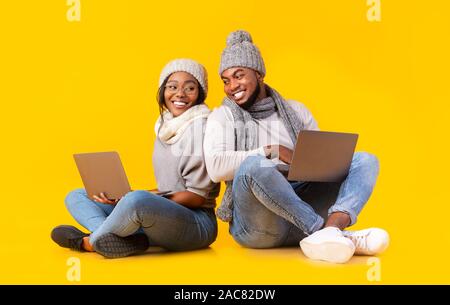 Smiling african millennial couple in winter hats browsing on laptops Stock Photo