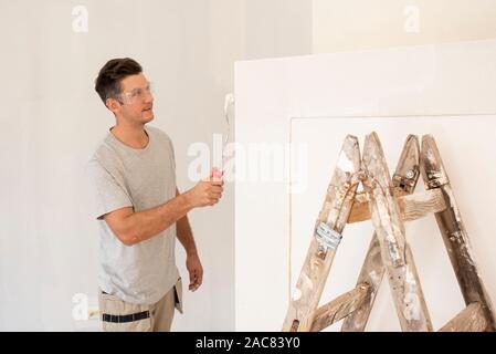 Shot of young handyman painting the wall while renovating apartment. Stock Photo