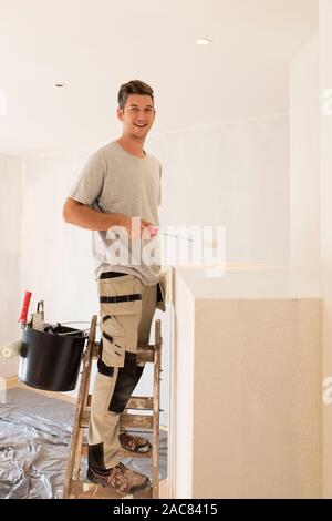 Shot of professional contractors standing on ladder and painting wall while refurbishing the apartment. Stock Photo