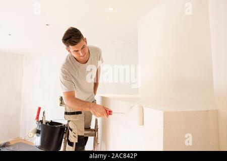 Shot of professional contractors standing on ladder and painting wall while refurbishing the apartment. Stock Photo