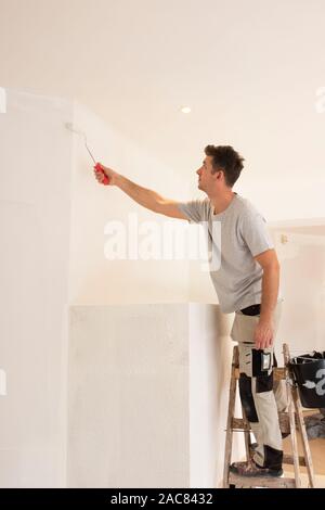 Shot of professional contractors standing on ladder and painting wall while refurbishing the apartment. Stock Photo