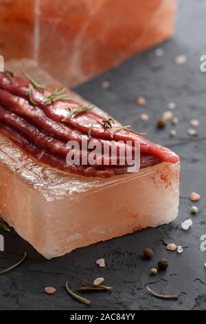 Cooking on salt block concept. Raw Black Angus beef marinated on Himalayan pink salt brick on black background side view copy space Stock Photo