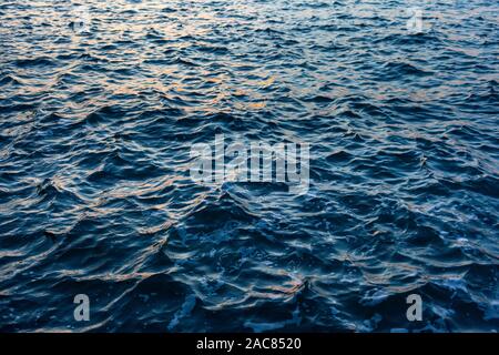 Dark blue Sea water with a choppy  texture and reflected orange highlights from a sunset Stock Photo