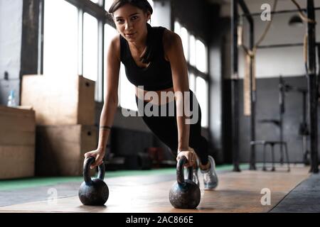 Slim brunette doing push-ups exercises on kettlebells. Cross fit training Stock Photo
