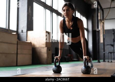 Slim brunette doing push-ups exercises on kettlebells. Cross fit training Stock Photo